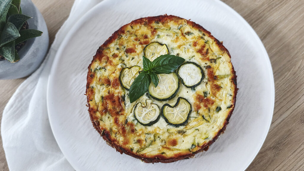 Torta di zucchine e ricotta chetogenica senza farina vista dall'alto, con fettine di zucchina e basilico fresco, 2,8g carb a fetta